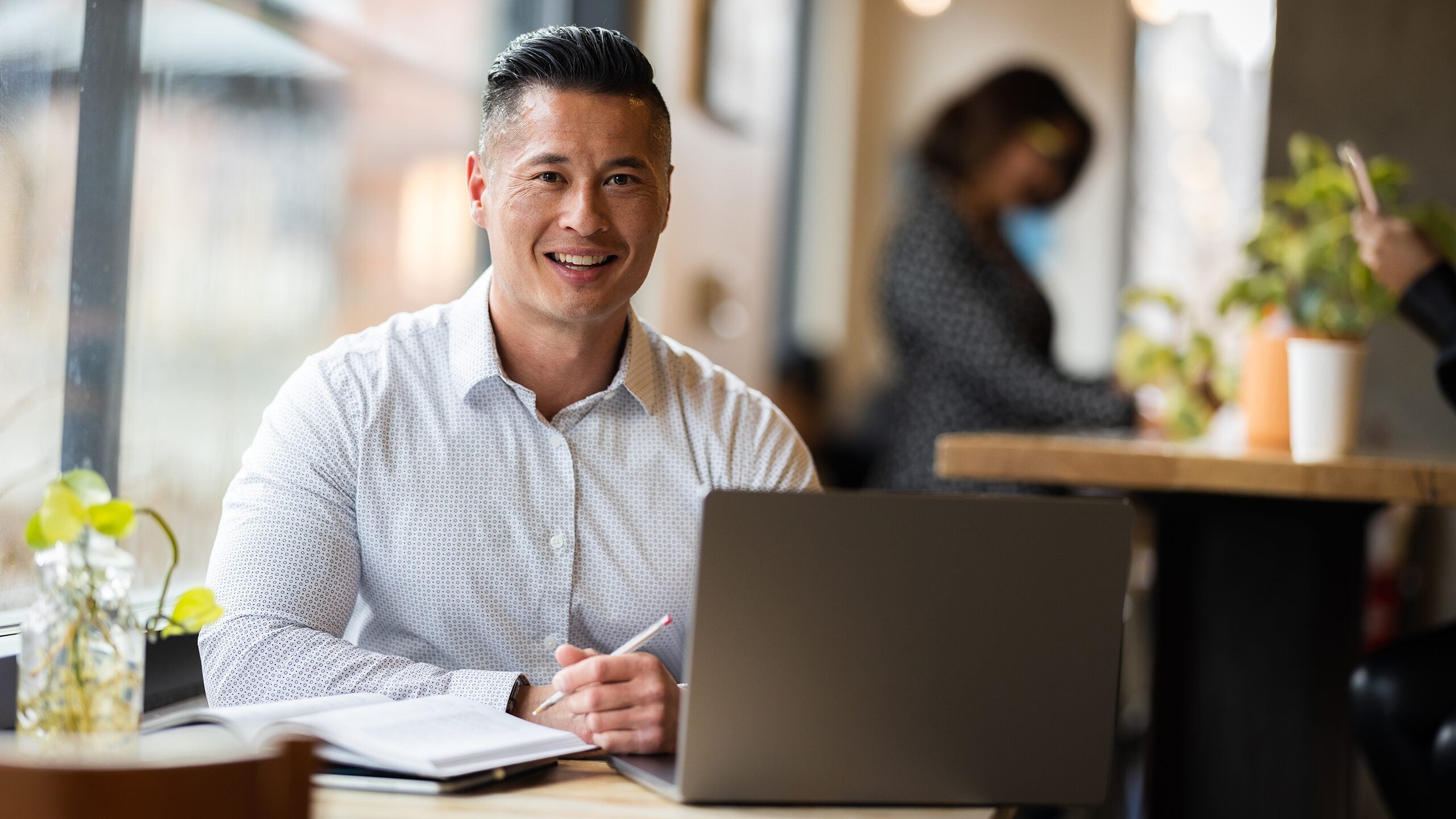 Smiling man studying on laptop while sitting in a cafe.