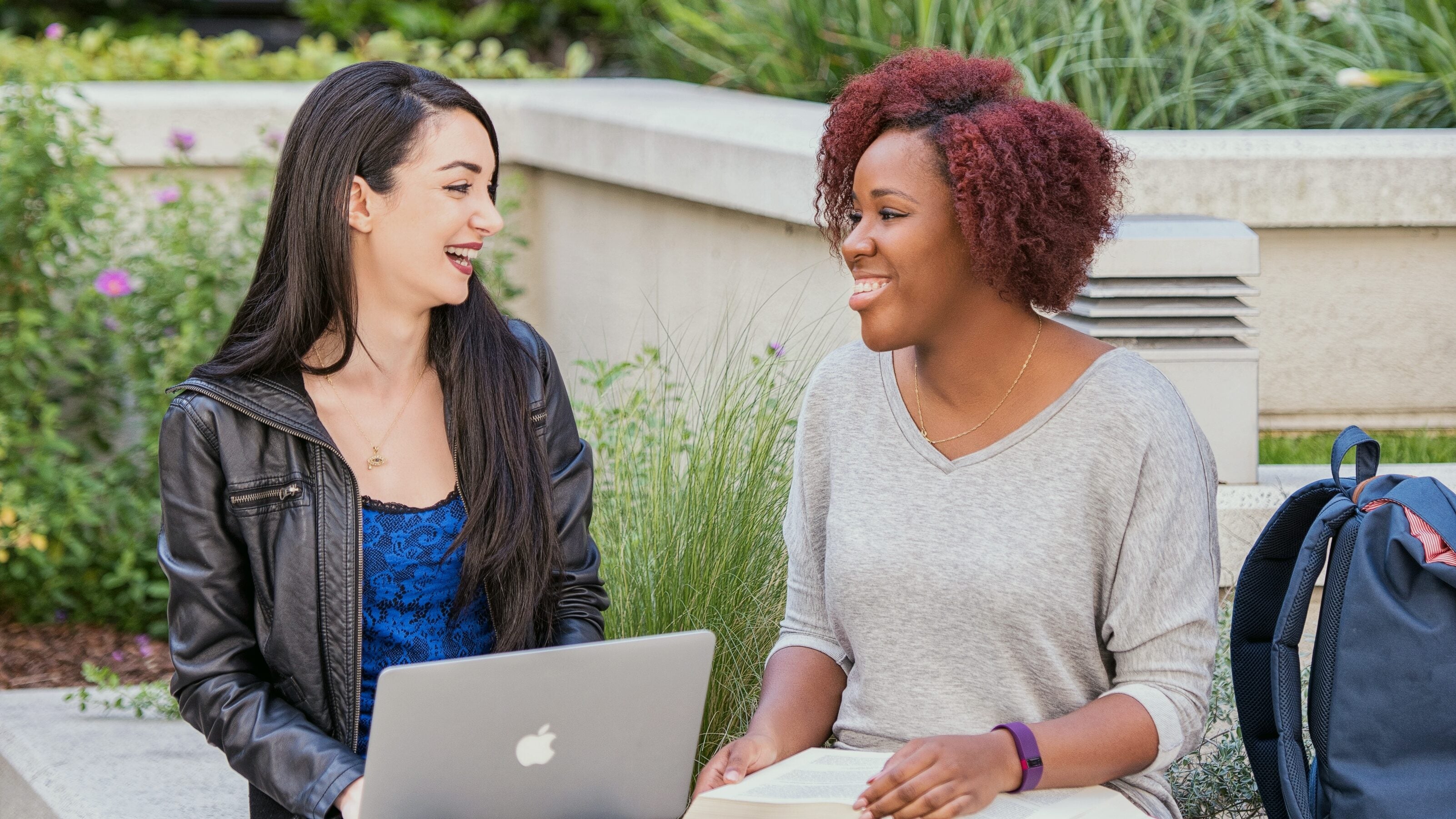 Classmates sitting outside together while working on a laptop and taking notes.