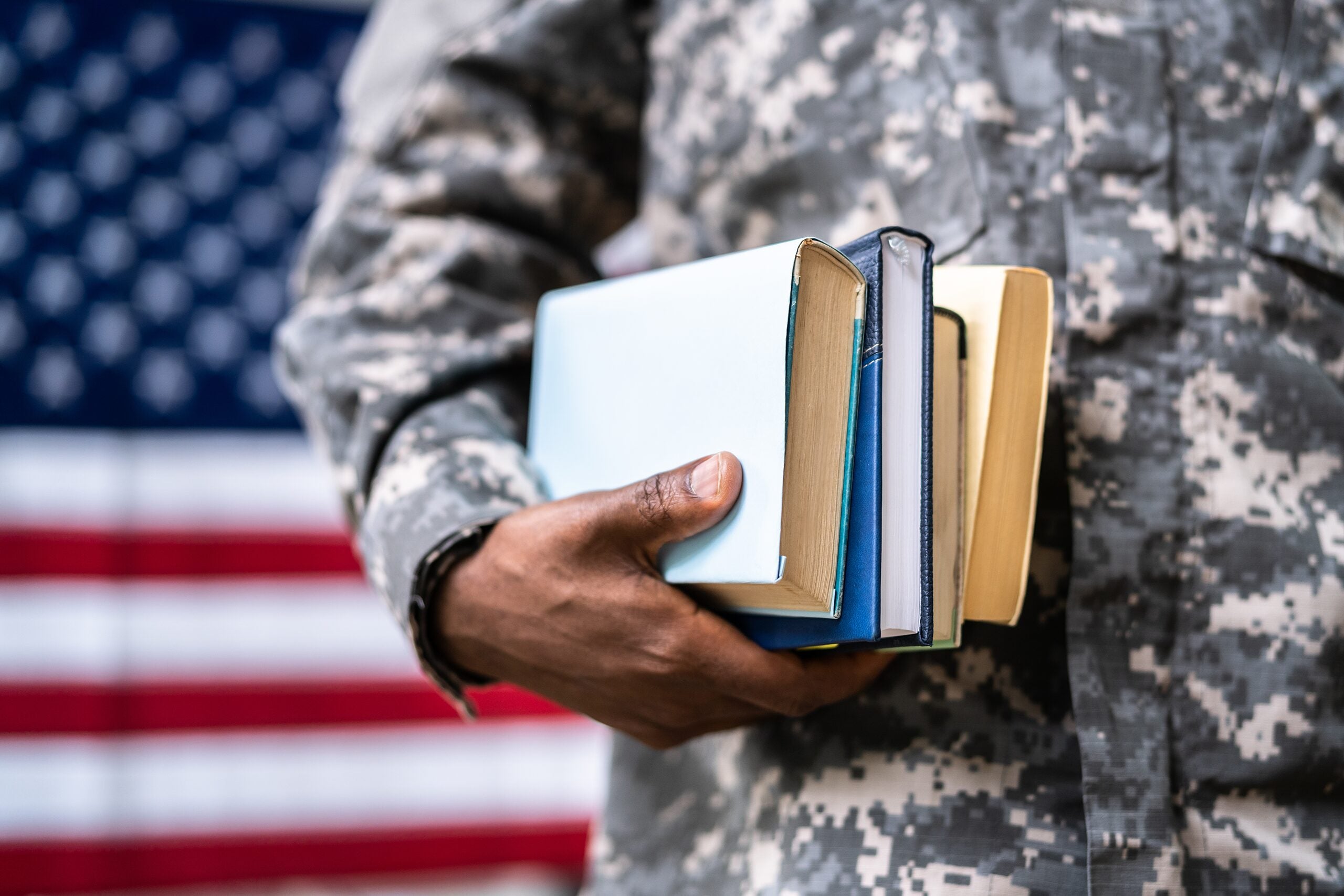Military student holding books and standing in front of an American flag.